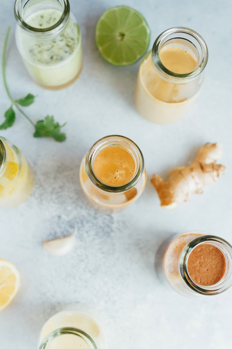 PIN THIS --> 6 HEALTHY homemade salad dressings that are super easy to make! 6 jars spread out on a grey countertop with a lime, ginger, cilantro, and garlic.