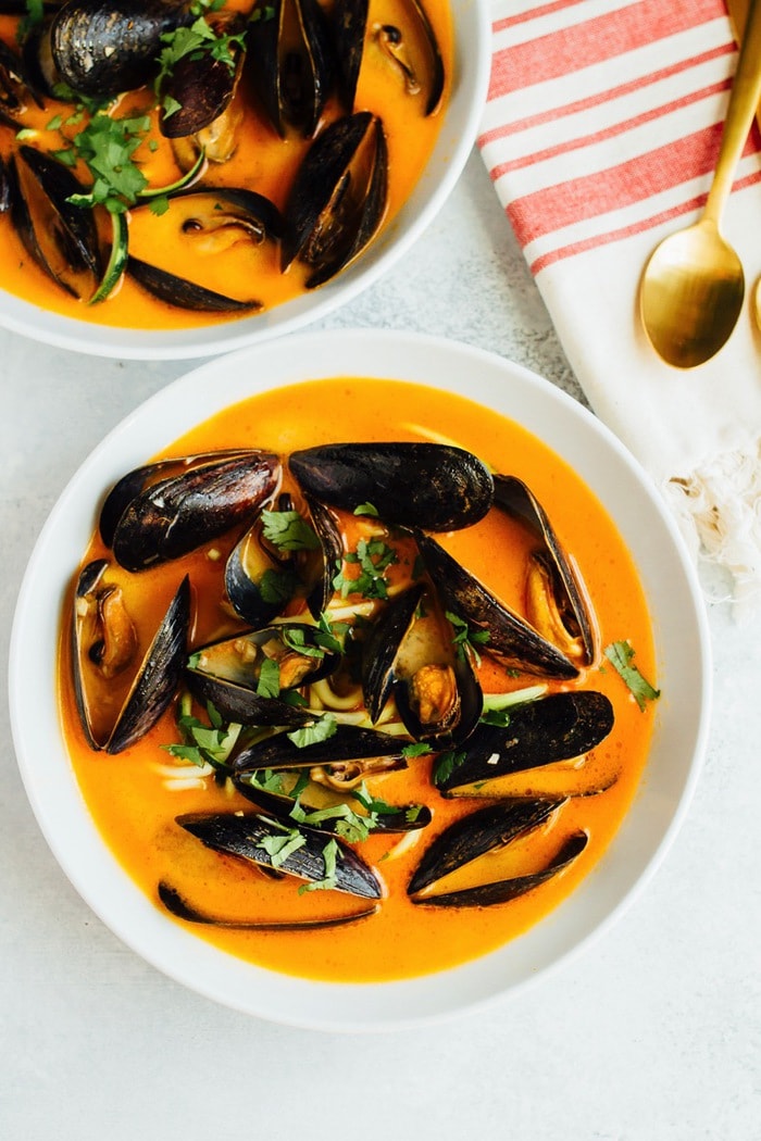 EASY COCONUT CURRY MUSSELS WITH ZUCCHINI NOODLES // paleo and gluten-free Two bowls of coconut curry mussels in a bowl with zucchini noodles and topped with cilantro.