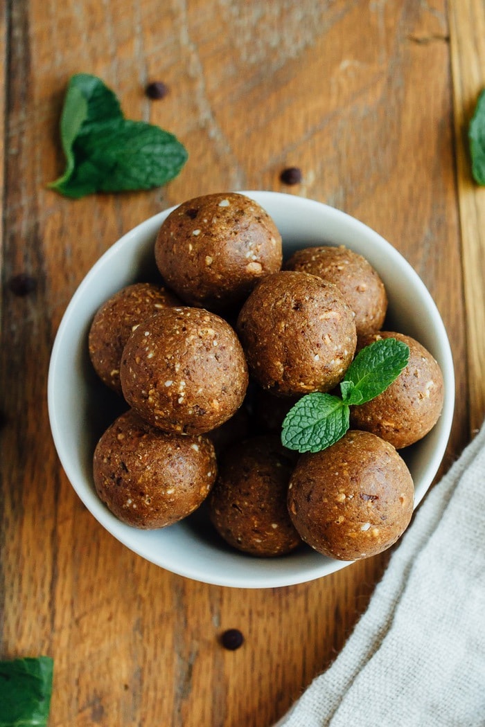 Thin Mint Protein Balls in a white bowl on wood cutting board with fresh mint leaves.