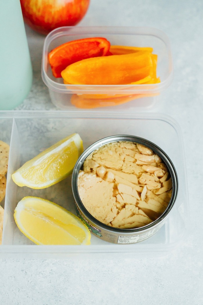 No time to pack lunch? Try this simple lemony tuna salad recipe you can make at your desk. Just add lemon juice, salt and pepper! Eat plain or serve with crackers and veggies. A can of tuna in a plastic container with two lemon slices. Another small container has bell peppers in it.