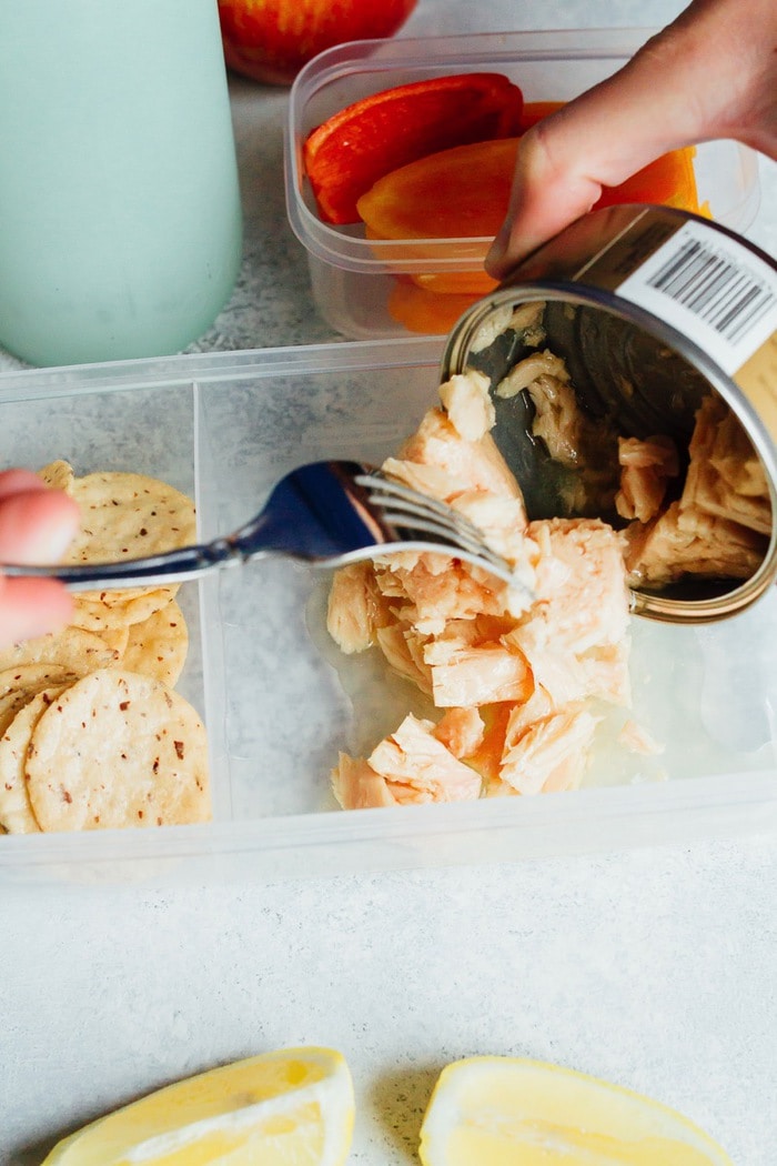 No time to pack lunch? Try this simple lemony tuna salad recipe you can make at your desk. Just add lemon juice, salt and pepper! Eat plain or serve with crackers and veggies. A fork scooping out the canned tuna into the meal prep container.