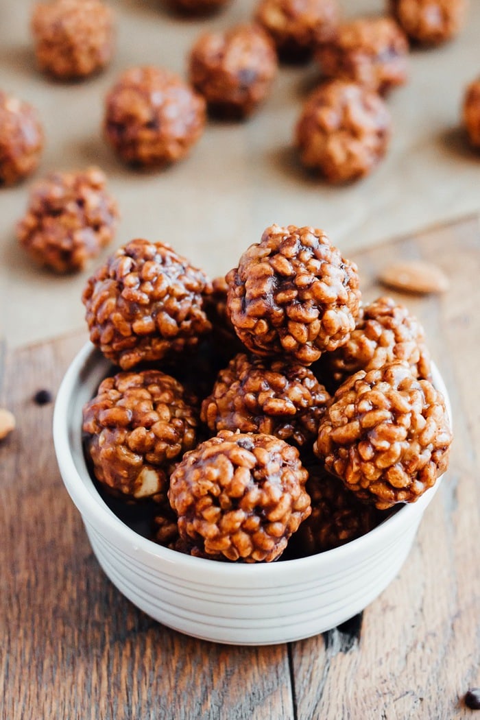 These chocolate almond crispy bites are dangerously good and made with only 5 ingredients. Perfect for kids (and adults), plus they’re vegan and gluten-free. An overflowing bowl of chocolate almond crispy bites is in the foreground, with a additional bites in the background resting on top of parchment paper.