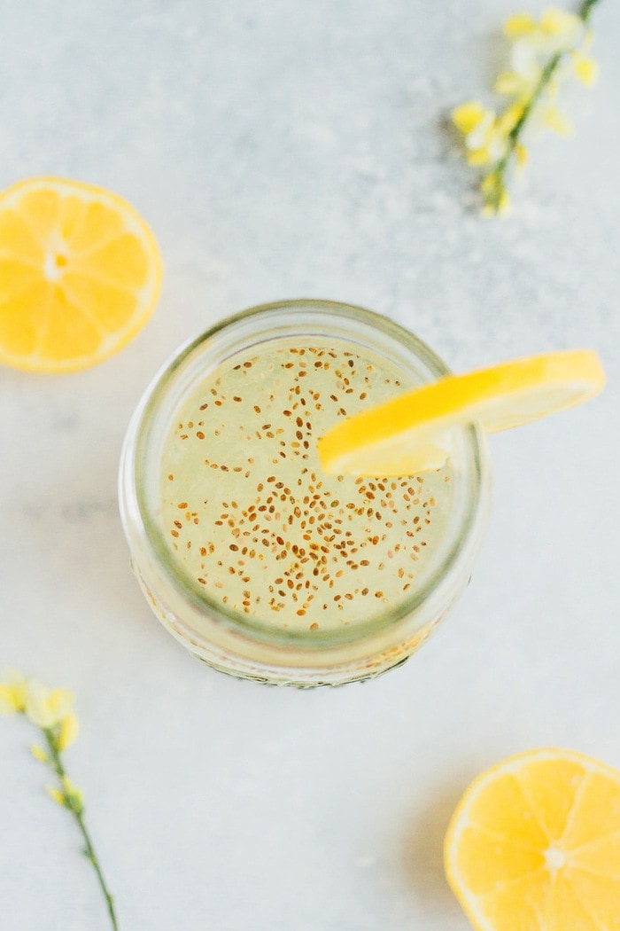 Lemon chia fresca in a mason jar with a lemon garnish and lemon slices on the table.