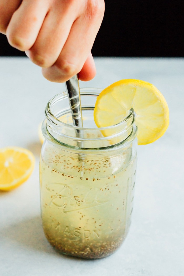 Hand stirring a spoon into a clear mason jar of Lemon Chia Fresca.