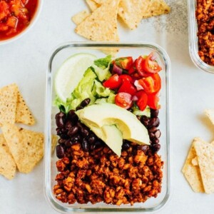 A glass container with tempeh, black beans, cherry tomatoes, lime, and lettuce.