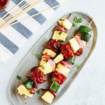 Three bbq tempeh skewers with onion, pineapple and zucchini on a plate.