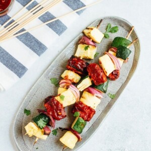 Three bbq tempeh skewers with onion, pineapple and zucchini on a plate.
