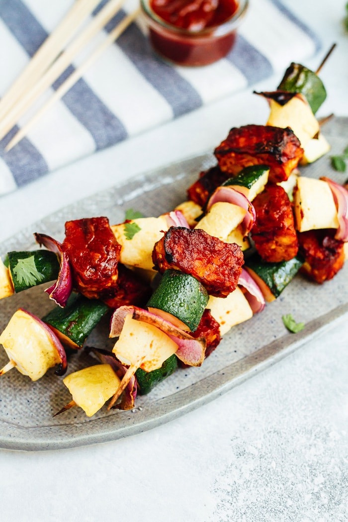 Bring on the BBQ tempeh skewers! You’ll love this plant-based grilling recipe where nutty tempeh is coated in homemade BBQ sauce and grilled to perfection with zucchini, summer squash and red onion. BBQ tempeh skewers with onion, pineapple and zucchini served a plate.
