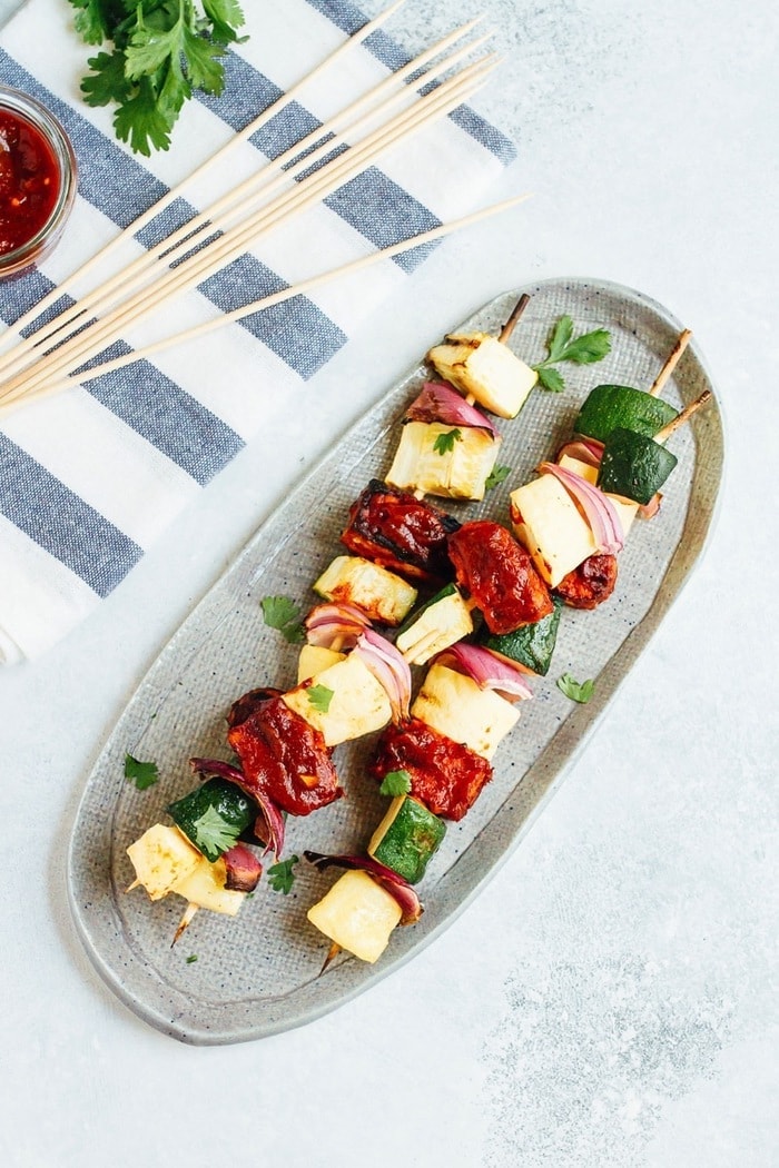 Bring on the BBQ tempeh skewers! You’ll love this plant-based grilling recipe where nutty tempeh is coated in homemade BBQ sauce and grilled to perfection with zucchini, summer squash and red onion. Three bbq tempeh skewers with onion, pineapple and zucchini on a plate.