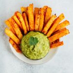 Jicama french fries served in a bowl with a guacamole dip in the center.