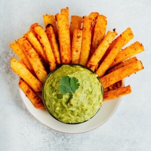 Jicama french fries served in a bowl with a guacamole dip in the center.