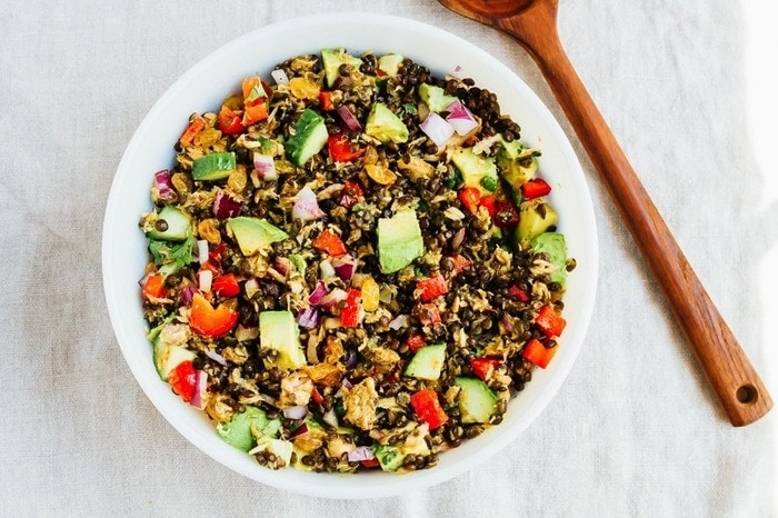 This lentil tuna salad combines beluga lentils with canned tuna, fresh veggies and a turmeric dressing. It's absolutely delicious and perfect for sharing at summer cookouts and parties. A large bowl of lentil tuna salad with a wooden serving spoon to the side of the bowl.