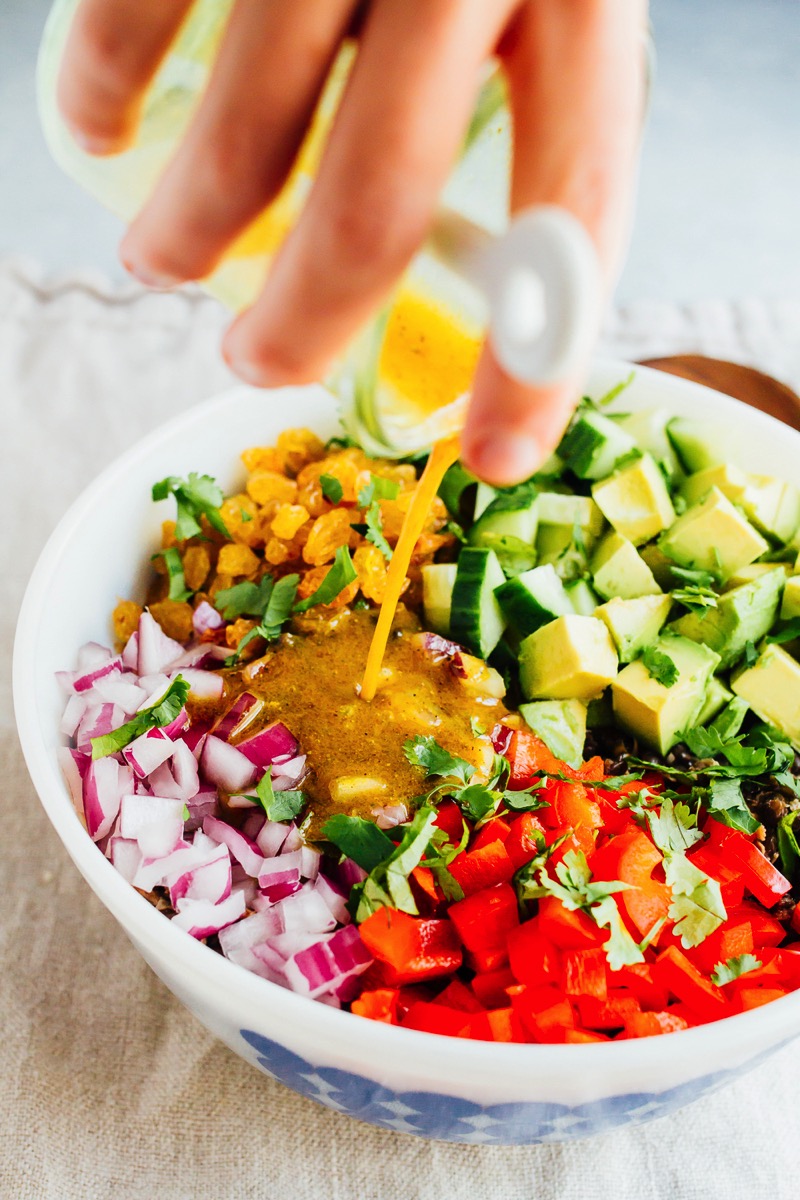 This lentil tuna salad combines beluga lentils with canned tuna, fresh veggies and a turmeric dressing. It's absolutely delicious and perfect for sharing at summer cookouts and parties. Dressing being poured over a lentil tuna salad with fresh vegetables.
