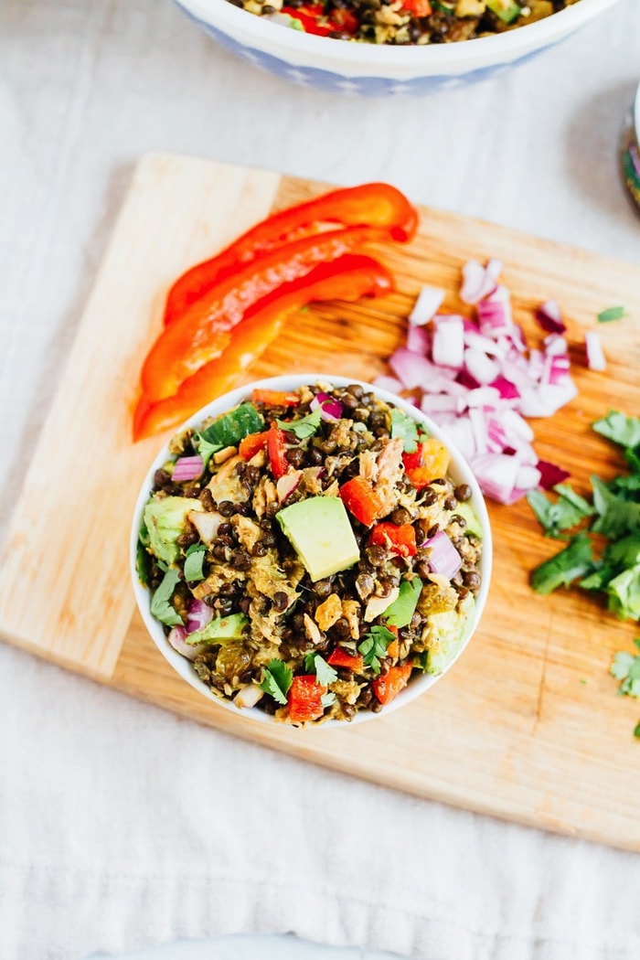 This lentil tuna salad combines beluga lentils with canned tuna, fresh veggies and a turmeric dressing. It's absolutely delicious and perfect for sharing at summer cookouts and parties. A serving of lentil tuna salad in a bowl on a wooden cutting board.