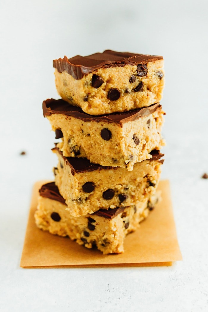 These no bake cookie dough bars have a base of grain-free chocolate chip cookie dough topped with layer of melted vegan chocolate. A stack of four no bake healthy cookie dough bars.