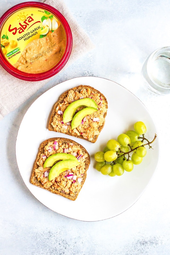 Combine hummus and bbq sauce with canned tuna for a sweet and savory open-faced bbq hummus tuna sandwich. It’s easy, healthy and absolutely delicious! Two slices of bread with tuna salad, and a side of green grapes. The tuna salad is topped with sliced avocado.