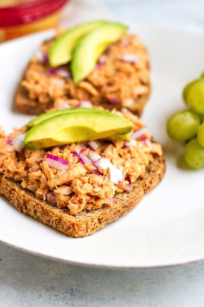 Combine hummus and bbq sauce with canned tuna for a sweet and savory open-faced bbq hummus tuna sandwich. It’s easy, healthy and absolutely delicious! A serving of tuna salad on two slices of bread topped with slice avocado and green grapes on the side.
