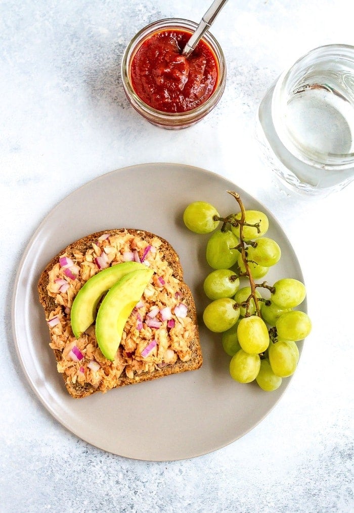 Combine hummus and bbq sauce with canned tuna for a sweet and savory open-faced bbq hummus tuna sandwich. It’s easy, healthy and absolutely delicious! A slice of bread with tuna salad, sliced avocado, and a side of green grapes all served on a plate.