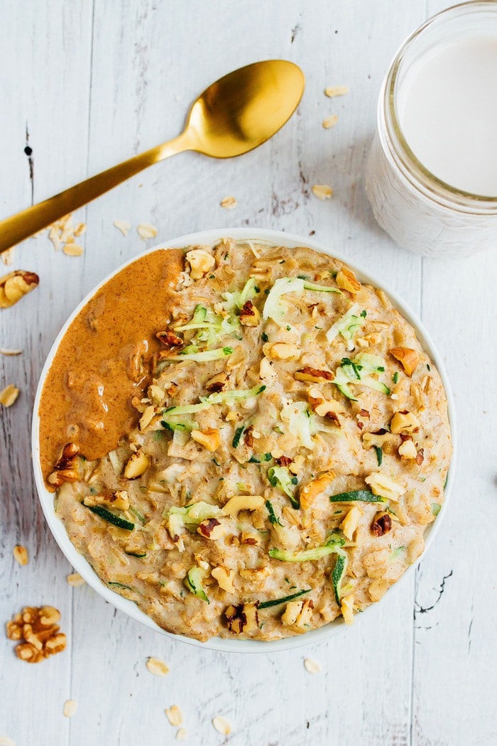 ZUCCHINI BREAD OATMEAL // vegan + gluten-free Bowl of zucchini bread oatmeal topped with walnuts and almond butter. Gold spoon and a glass of almond milk are next to the bowl.