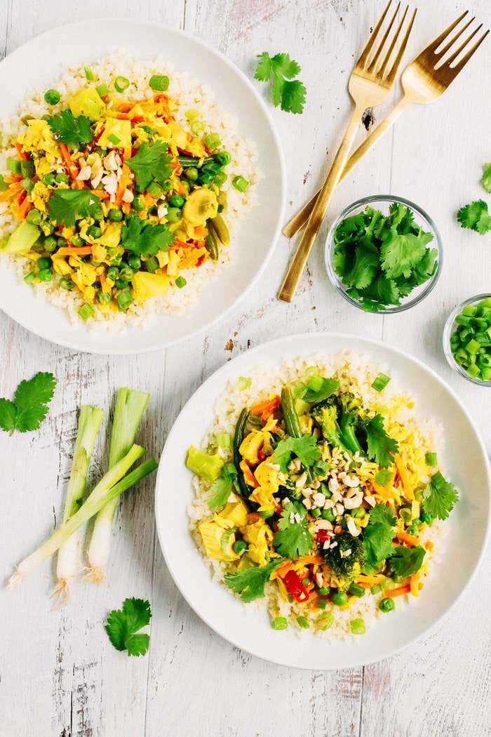 PIN THIS--> Tuna Curry Bowl with Cauliflower Rice Two bowls of tuna curry with cauliflower rice, filled with green veggies and topped with cilantro and chopped peanuts. Bowls on a table next to green onions, two forks, and cilantro.