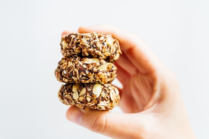 Eat like a bird with these BIRD FOOD ENERGY BITES! Made with whole grain oats, nuts, seeds and dried fruit, these bites are a nutrient-rich treat perfect for on-the-go snacking. Vegan + gluten-free. Hand holding three granola bites.
