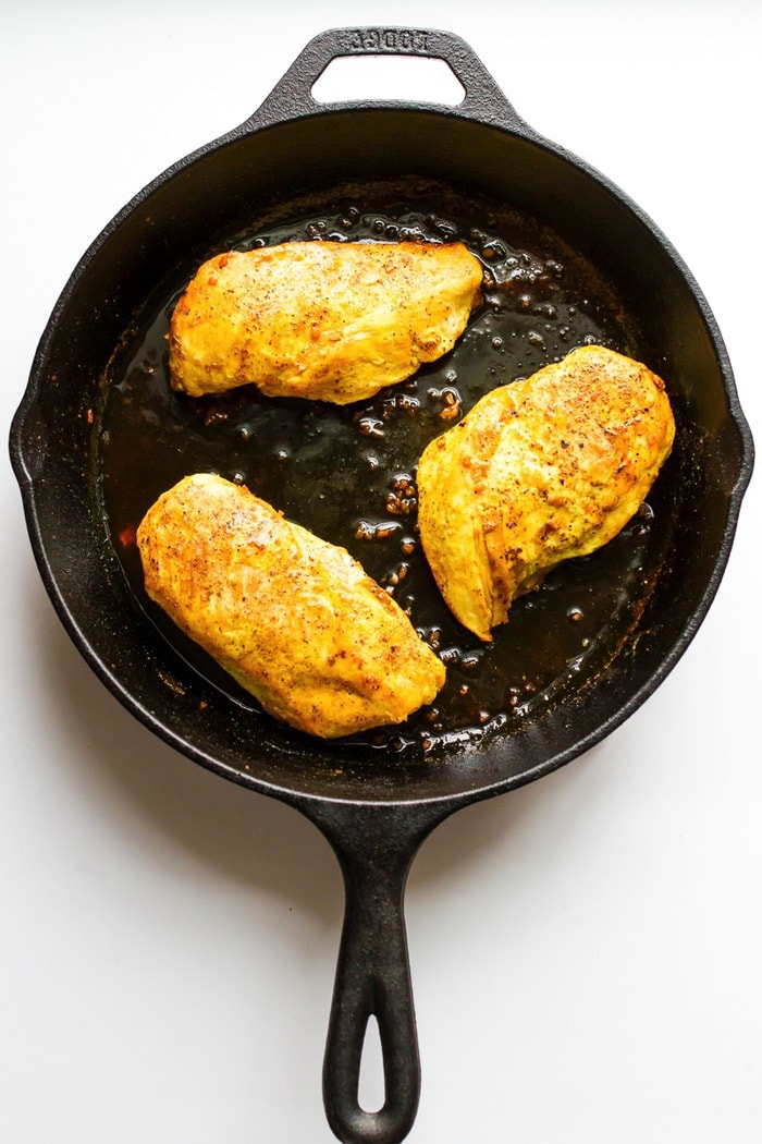 Overhead photo of maple turmeric chicken in cast-iron skillet, white background.