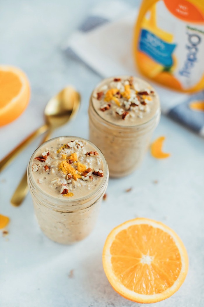 Orange Vanilla Overnight Oats // Vegan + Gluten-Free Two servings of overnight oats in mason jars and tops with pecans and orange zest with a split orange nearby.