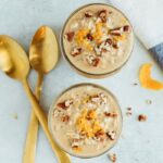 Two glass jars served with overnight oats and topped with crushed pecans and orange zest.