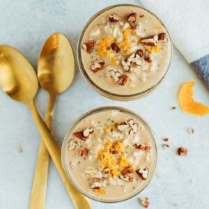 Two glass jars served with overnight oats and topped with crushed pecans and orange zest.