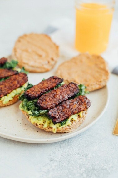 A breakfast sandwich on a plate with avocado, kale, and tempeh.