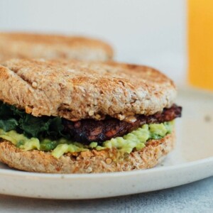 A vegan breakfast sandwich loaded with all the goods: creamy avocado, almond butter, sautéed kale and tempeh bacon, served on a perfectly toasted english muffin.