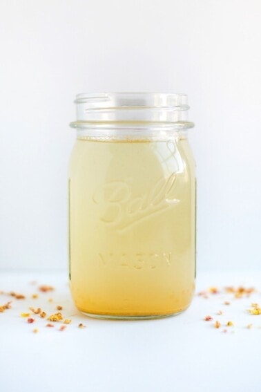 A glass mason jar containing a ginger spice apple vinegar drink.