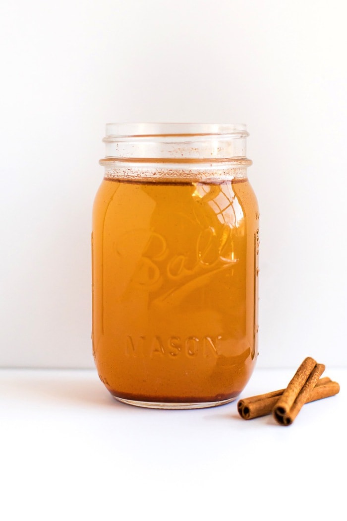 Apple Pie Apple Cider Vinegar Drink A glass mason jar with an apple pie vinegar drink with two cinnamon sticks to the side of the jar.