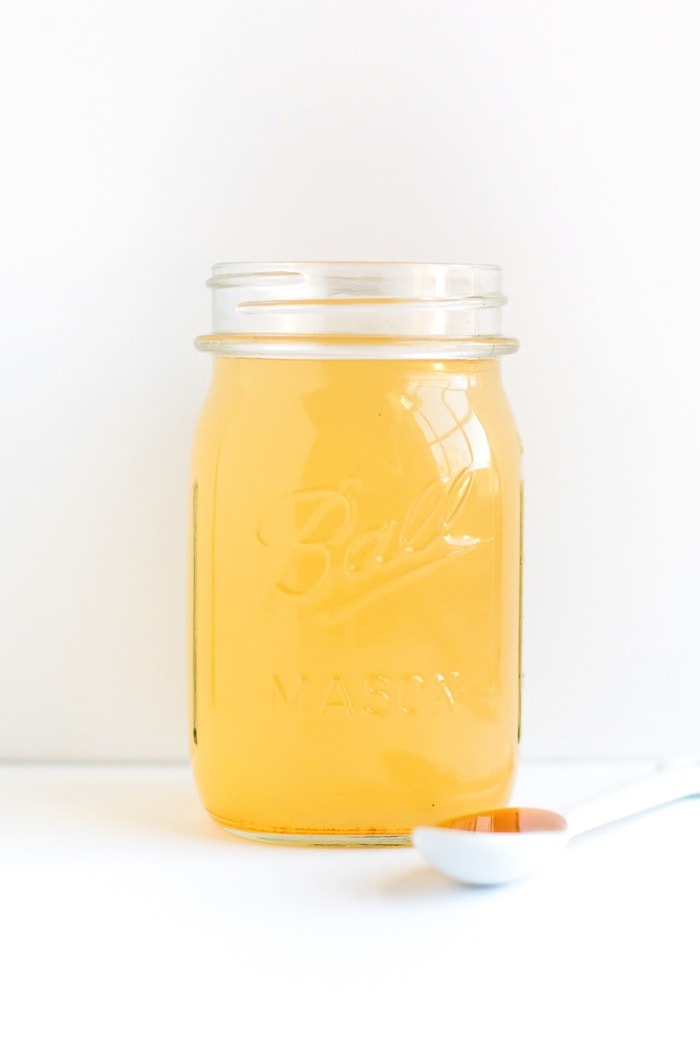 Honey Cayenne Apple Cider Vinegar Drink A glass mason jar of a honey cayenne apple vinegar drink with a spoon of honey next to the jar.