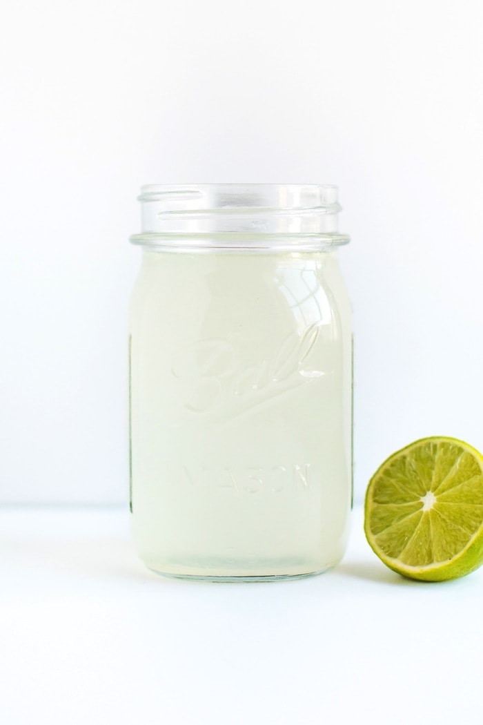 Limeade Apple Cider Vinegar Drink A glass mason jar containing a limeade vinegar drink with a half of a lime next to the jar.