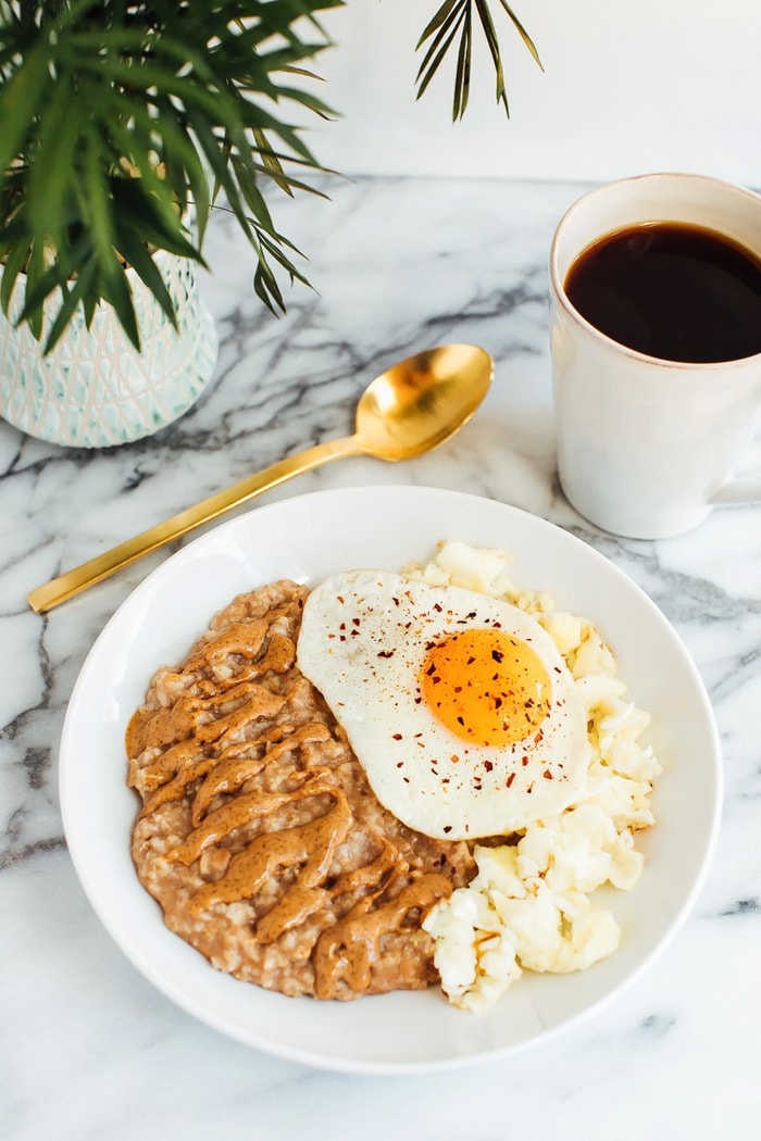 A serving of oatmeal, cauliflower, and an egg in a bowl with a cup of coffee to the side.