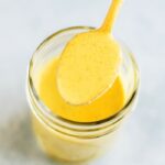 A spoonful of turmeric tahini dressing over a mason jar of the dressing.