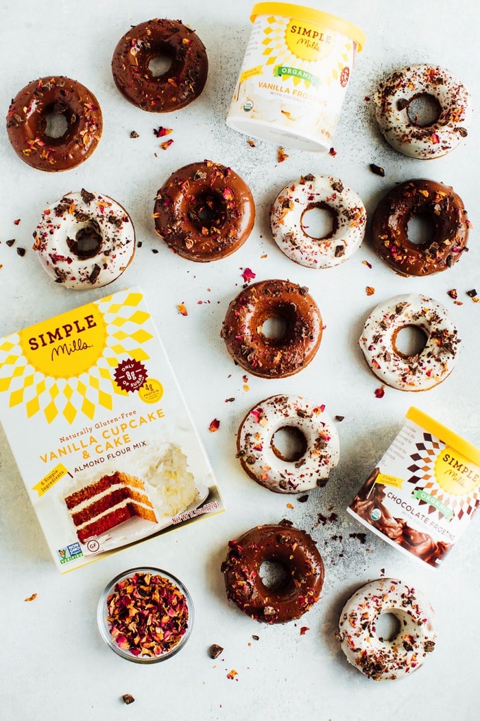 Perfect for Valentine’s Day, these baked almond flour donuts with rose petals and dark chocolate are gluten-free, dairy-free and naturally sweetened with coconut sugar. Baked almond flour donuts topped with rose petals on a counter top near a Simple Mills box of vanilla cupcake and cake almond flour mix.