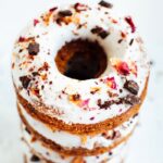 A stack of almond flour donuts topped with chocolate and rose petals.