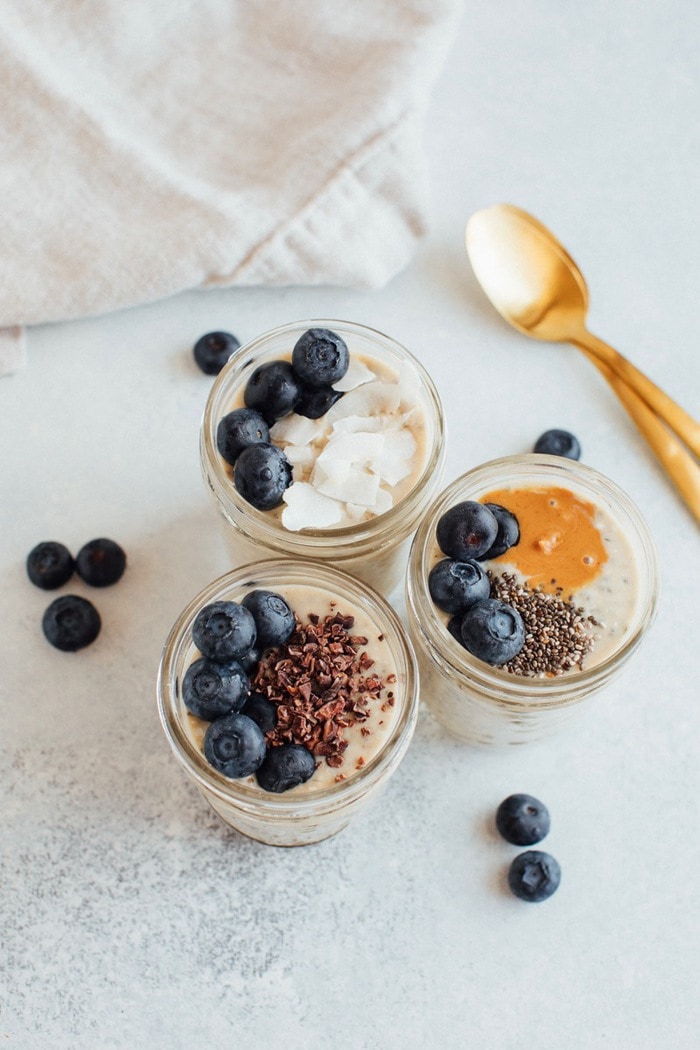Three pint size mason jars with grain-free overnight "oats" topped with blueberries, cacao nibs, chia seeds and coconut. Three pint size mason jars with grain-free overnight "oats" topped with blueberries, cacao nibs, chia seeds and coconut.