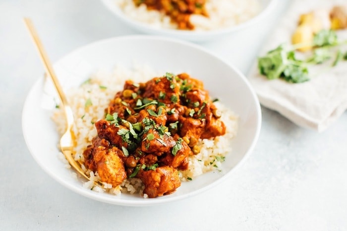 Tempeh tikka masala with chickpeas on cauliflower rice on a white plate.