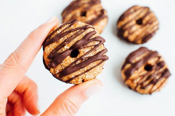 Hand holding one homemade Samoas cookie with three cookies in the background. Hand holding one homemade Samoas cookie with three cookies in the background.