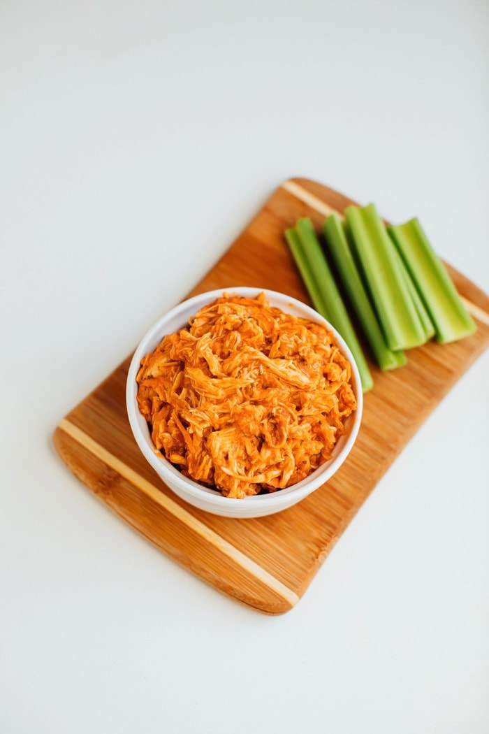 Slow cooker shredded buffalo chicken in a bowl with celery sticks on the side. Slow cooker shredded buffalo chicken in a bowl with celery sticks on the side.