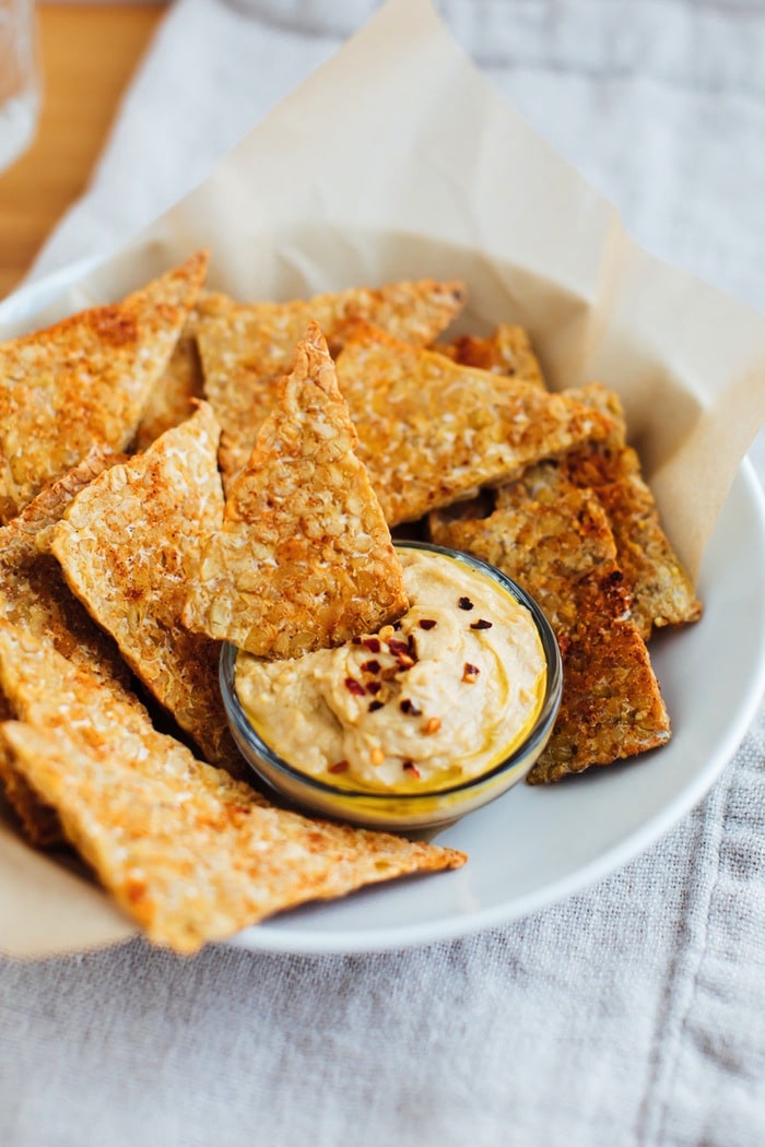 Baked tempeh chips in a white bowl with hummus. Baked tempeh chips in a white bowl with hummus.