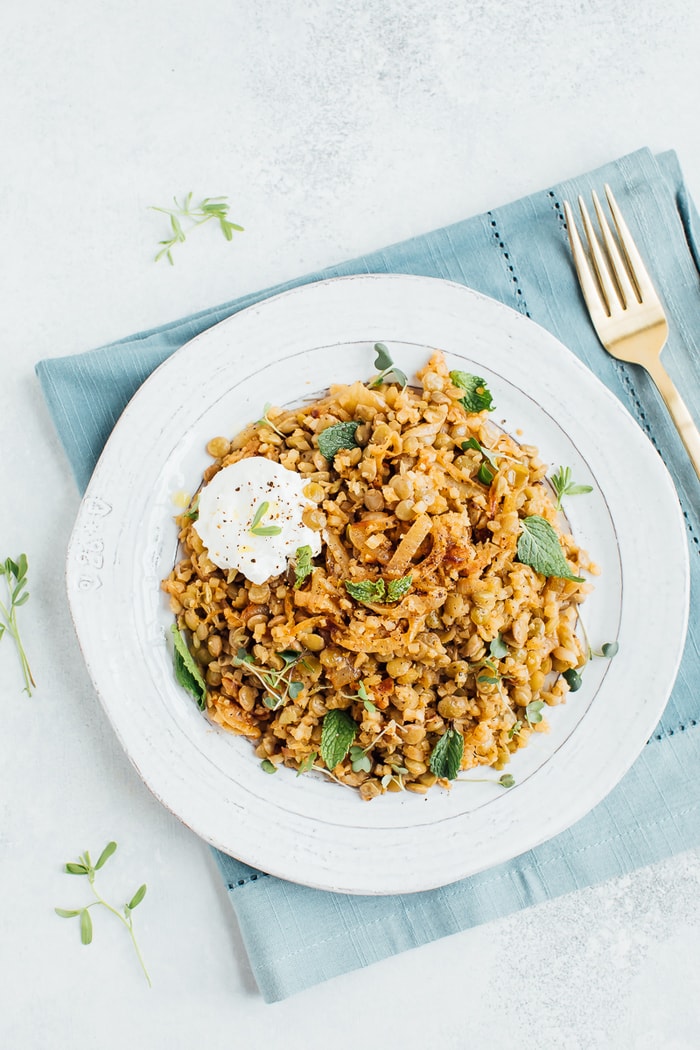 Pin this recipe for lightened up Mujadara with low-carb cauliflower rice instead of regular rice! Caramelized onions, lentils and cauliflower rice on a rustic plate with a gold fork in the background.