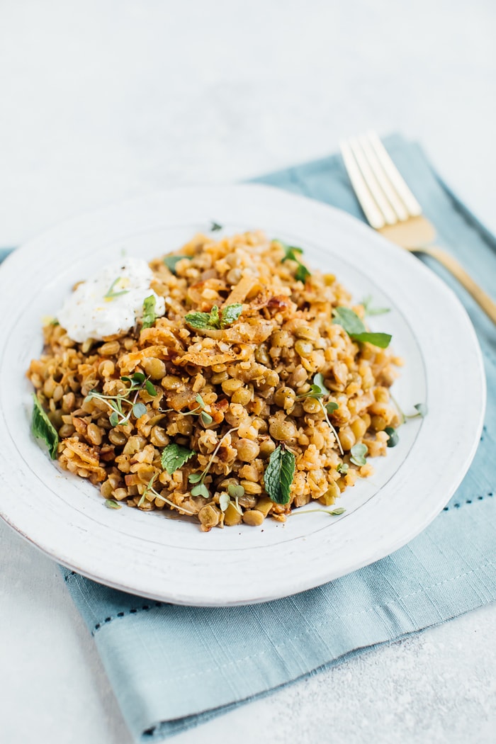 Pin this recipe for lightened up Mujadara with low-carb cauliflower rice instead of regular rice! Caramelized onions, lentils and cauliflower rice on a rustic plate with a gold fork in the background.