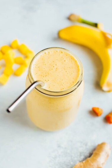 Golden milk smoothie surrounded by mango chunks, banana, and ginger.
