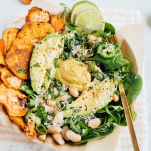 A serving of loaded sweet potato nacho salad with sweet potato chips, beans, baby spinach, jalapeño and fresh herbs.