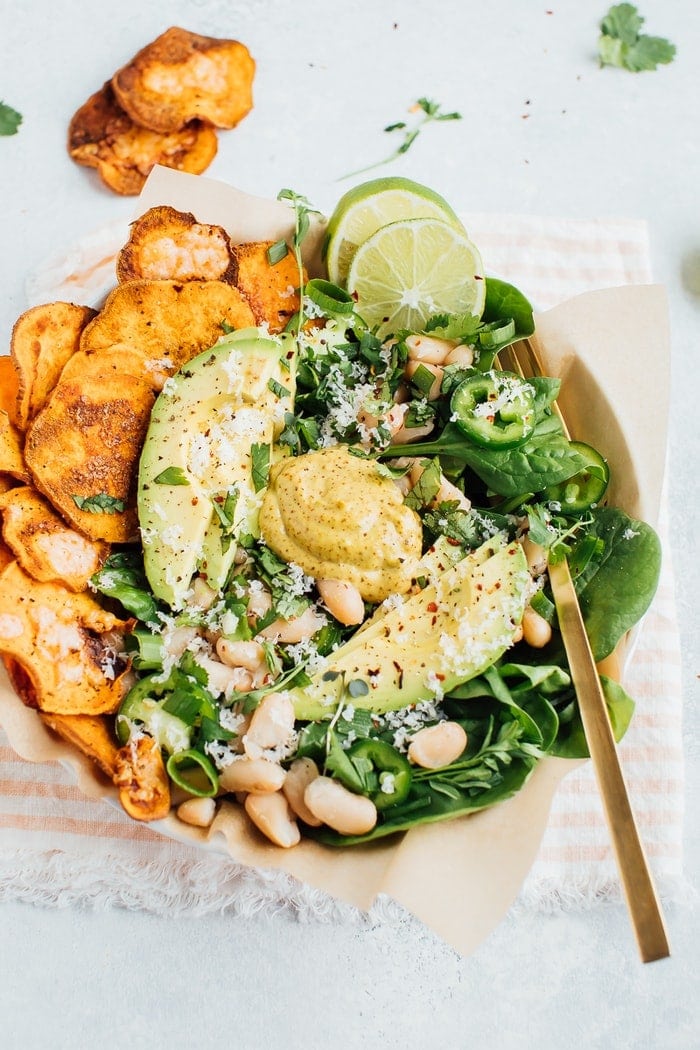 A serving of loaded sweet potato nacho salad  with sweet potato chips, beans, baby spinach, jalapeño and fresh herbs.