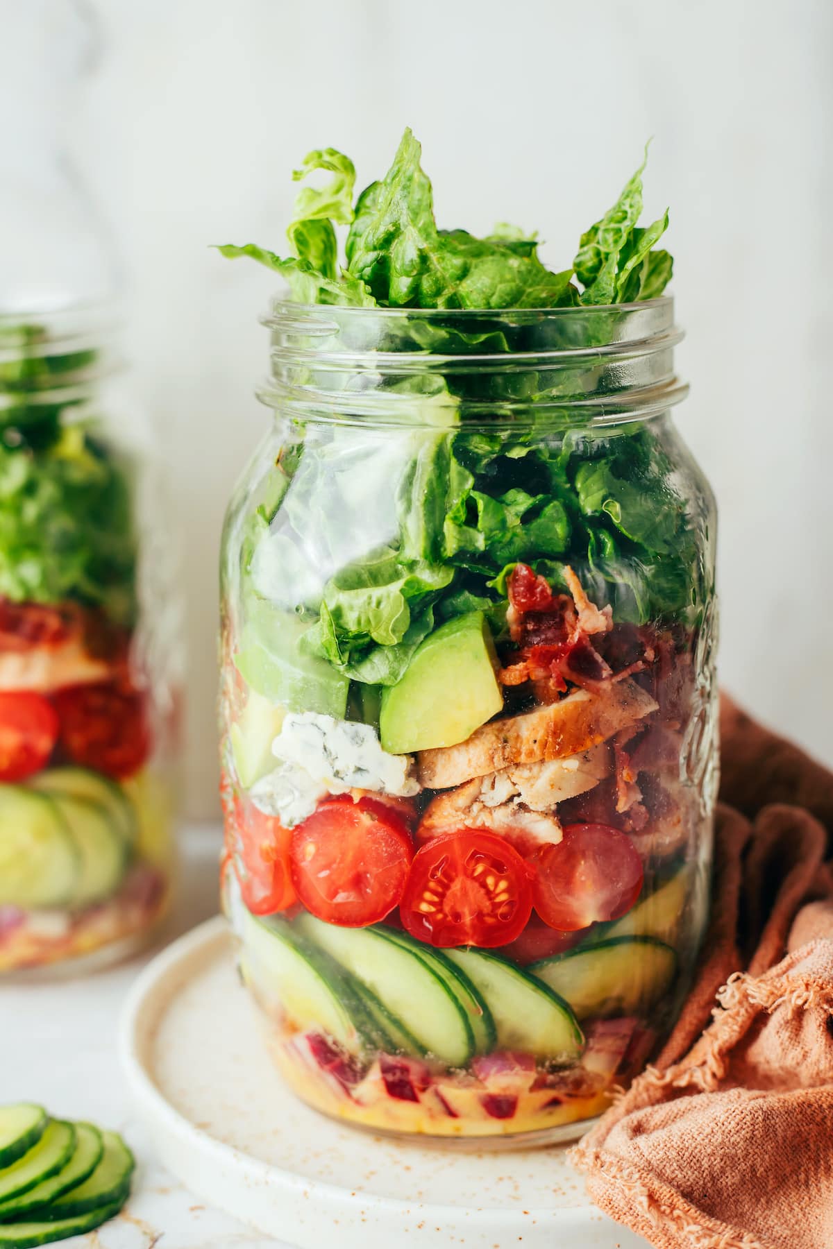 A glass mason jar layered with sliced cucumber, cherry tomatoes, chicken, avocado, and lettuce.